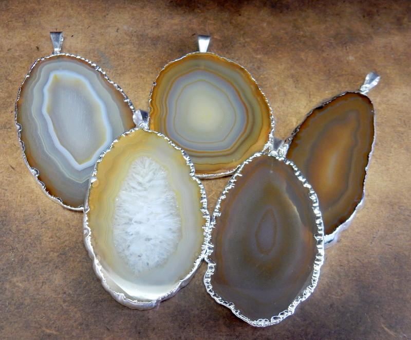 Picture of natural color agate slice pendants being displayed on a dark brown background.