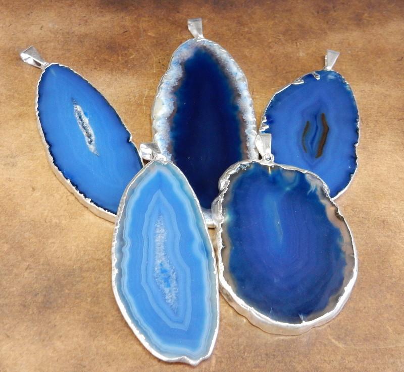 Picture of our blue agate slice pendants being displayed on a dark brown background.