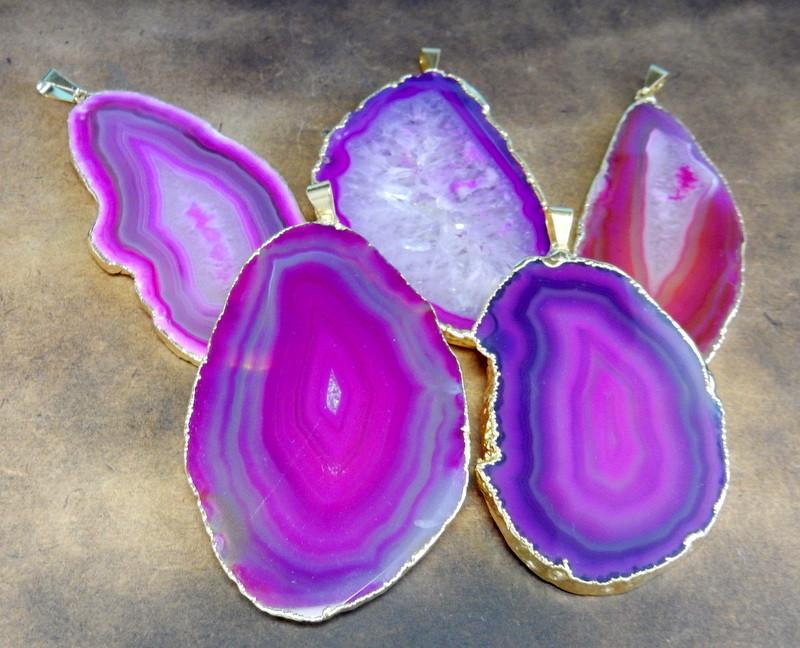 Picture of our pink /agate slice pendants being displayed on a dark brown background.