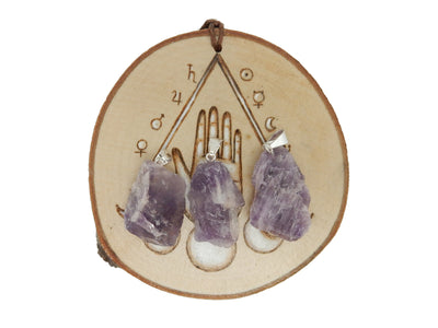 3 amethyst Rough Stone Pendants with silver bails on wooden coaster