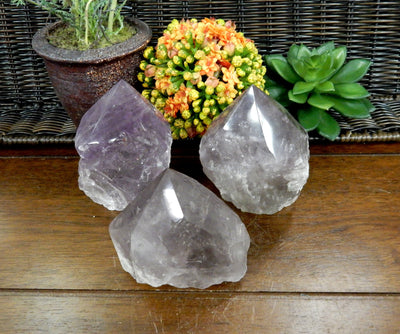 3 Raw Amethyst Semi Polished Points on wooden table with various decorations in the background