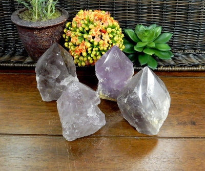 4 Raw Amethyst Semi Polished Points on wooden table with various decorations in the background