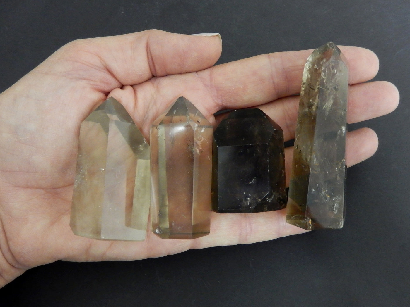 four 40g - 80g smokey quartz polished points in hand over black background for size reference and possible variations