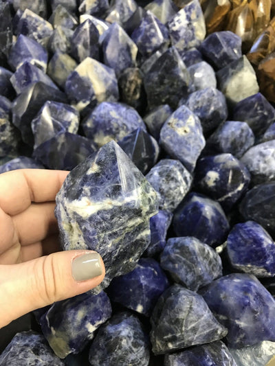 hand holding up sodalite semi polished point with many others in the background