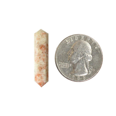 sunstone double terminated point next to a quarter for size reference on white background