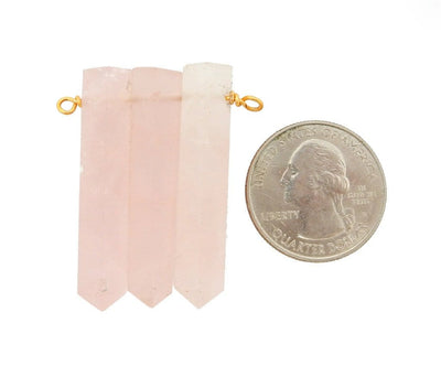 A Triple Rose Quartz Pencil Point Pendant With Gold Plated Wire Bails next to a quarter for size reference
