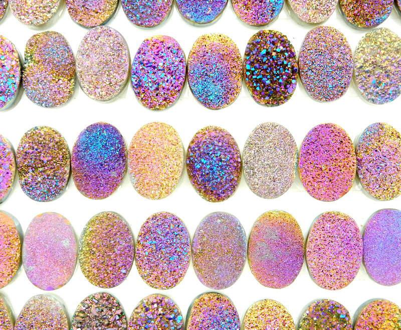 Various Purple And Yellow Oval Druzy Cabochons lined up on a white surface.