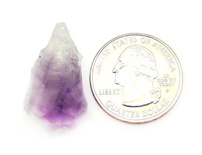 Raw Amethyst Point next to quarter for size comparison on white background