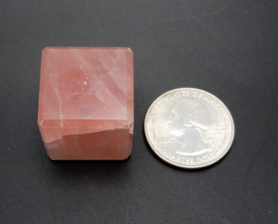 Rose Quartz Cube next to a quarter for size comparison on black background