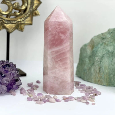 Rose Quartz Polished Point Tower on a table with items around it