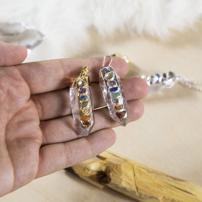 hand holding up 2 Crystal Quartz Point Pendants in gold and silver