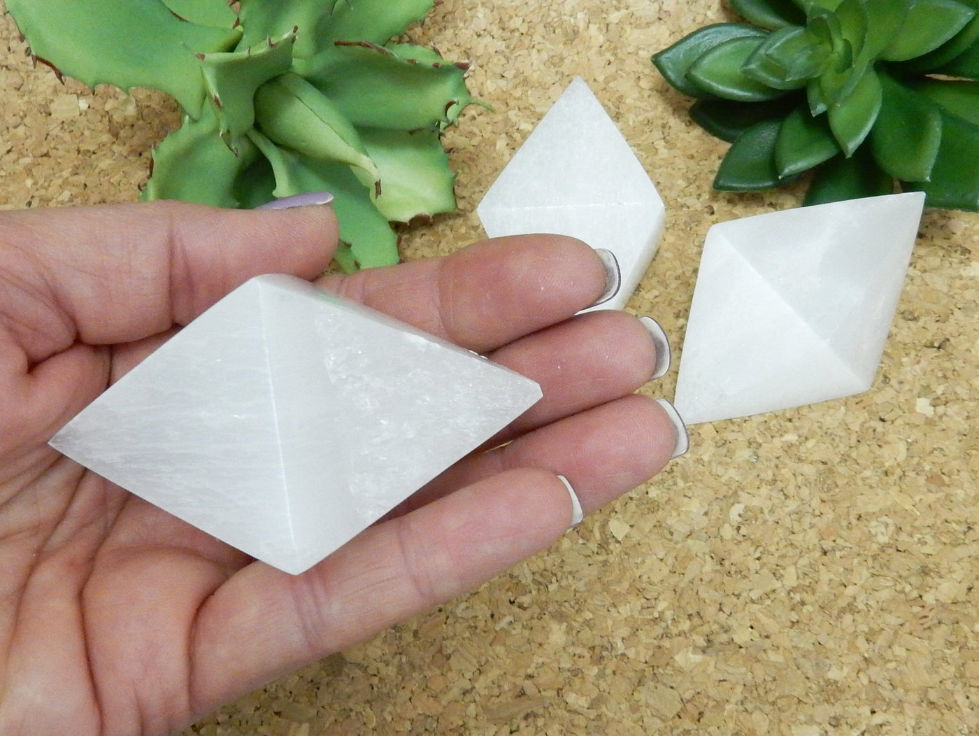 selenite double pyramid in hand for size reference with others in background