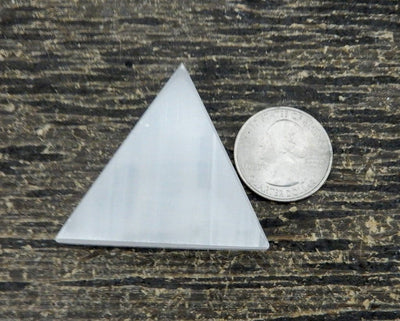 close up of one selenite triangle with quarter for size reference