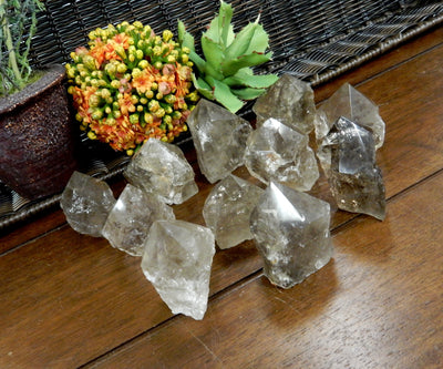 Angled shot of  Smokey Quartz Semi Polished Points on wooden table with plants in the background