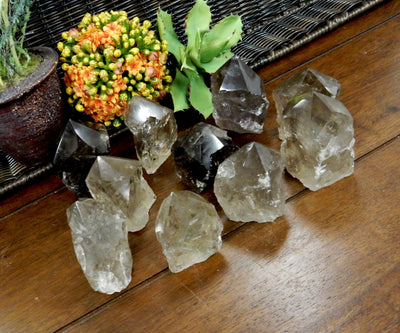 Angled shot of  Smokey Quartz Semi Polished Points on wooden table with plants in the background