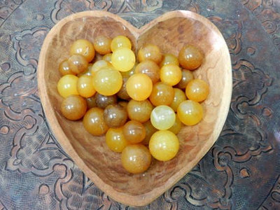 A hearts shaped bowl holding a pile of Yellow Onyx Spheres Petite Size 