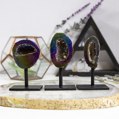 3 Rainbow Aura Geodes on Stands with various items blurred in the background