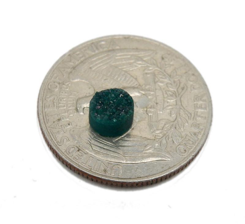 A Teal Green Round Druzy piece on top of a quarter for sizing .