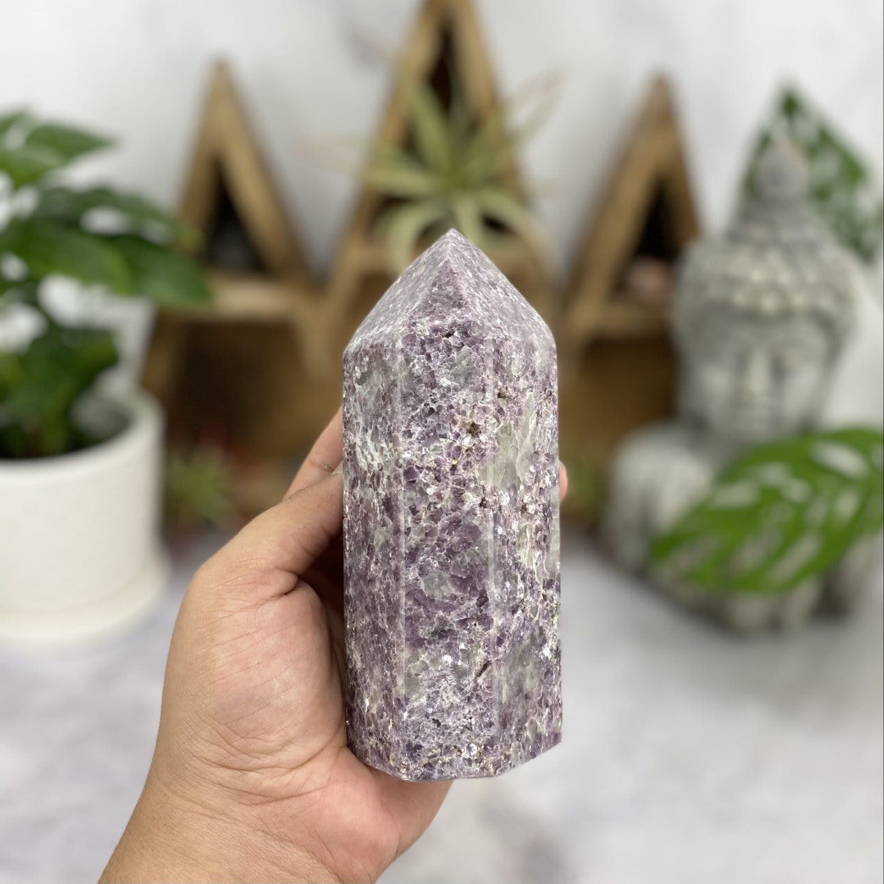hand holding up Lepidolite Point Polished Tower with decorations in the background