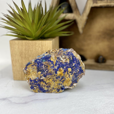 Raw Azurite with Malachite on marble table with plants and decorations blurred in the background