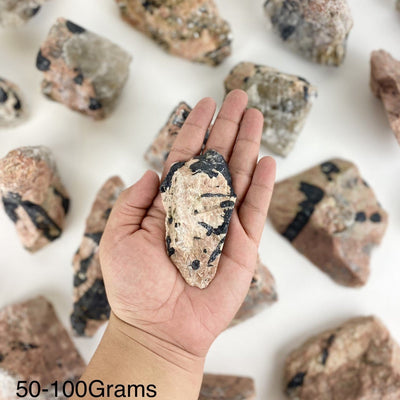 One piece of Feldspar with Black Tourmaline in the hand showing the weight of 50 to 100 grams.