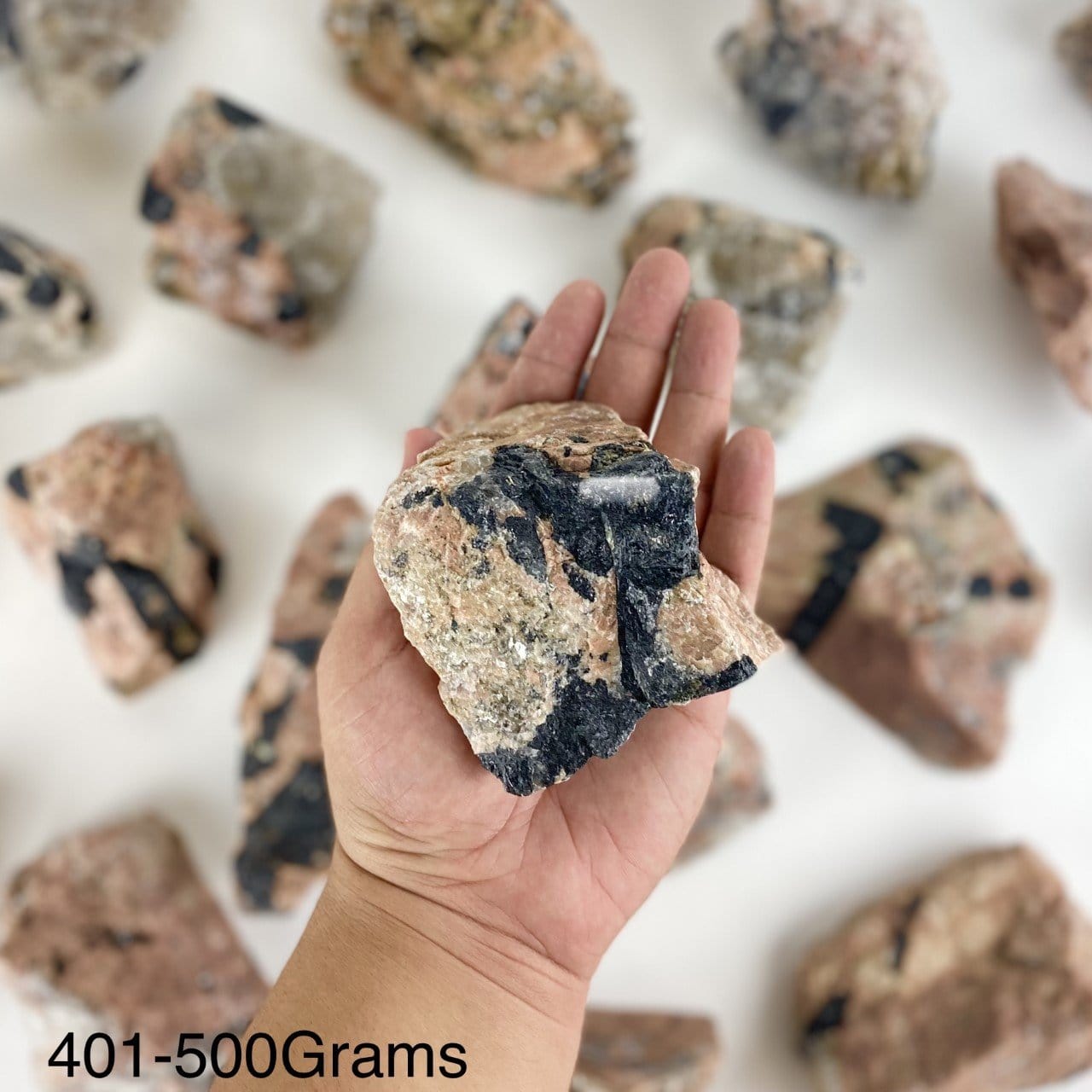One piece of Feldspar with Black Tourmaline in the hand showing the weight of 401-500 grams.