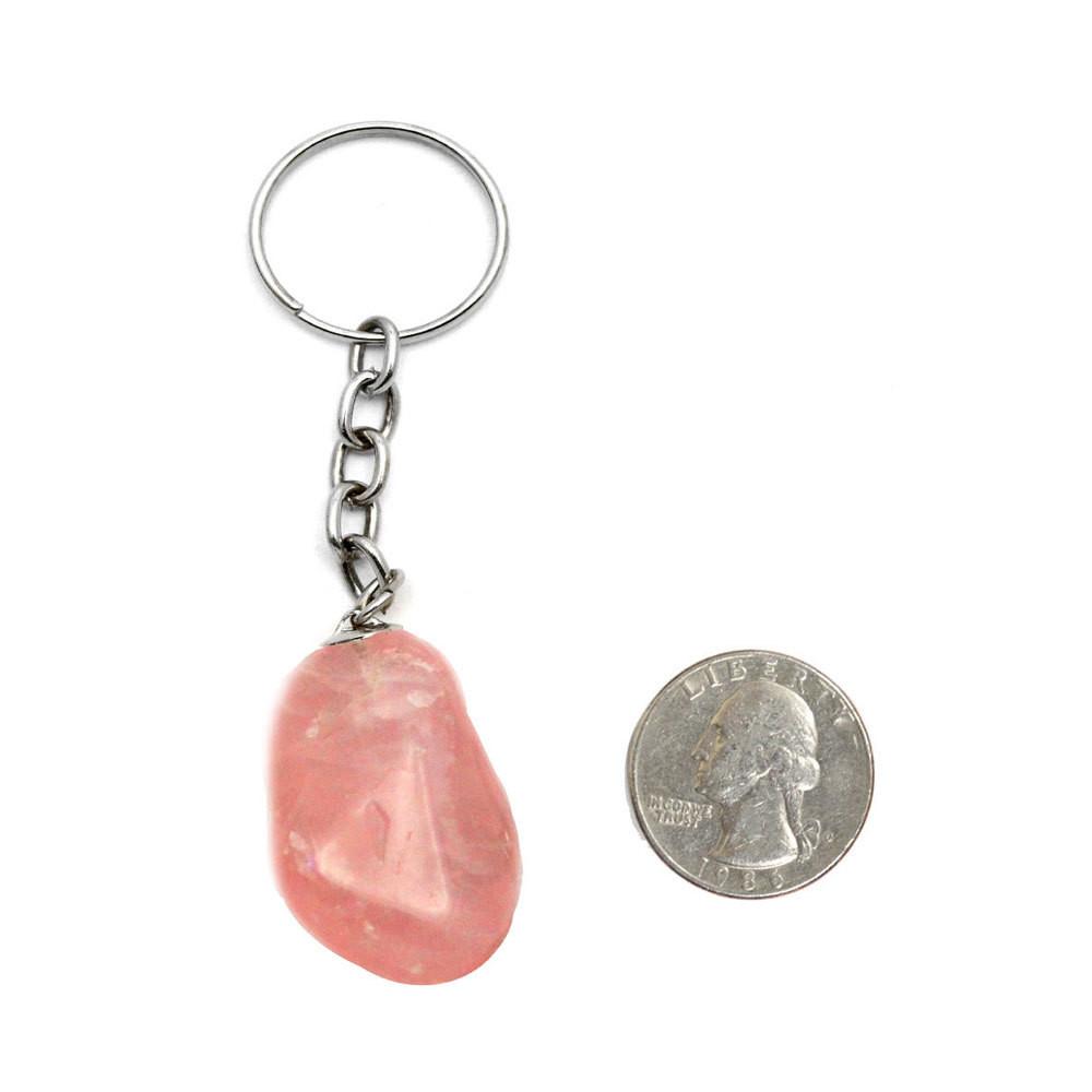 tumbled rose quartz keychain next to a quarter for size reference on white background