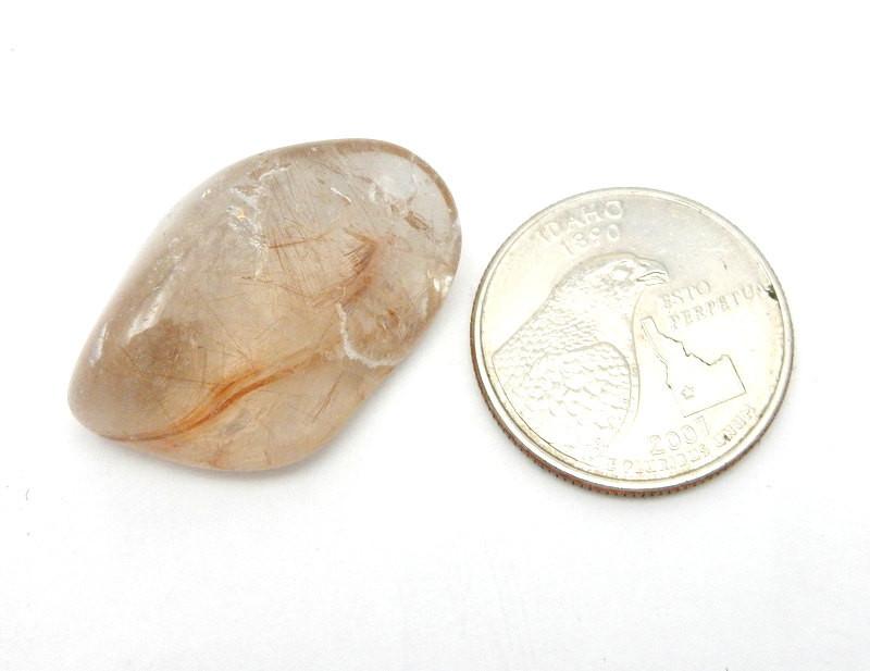 tumbled rutilated quartz next to a quarter for size reference