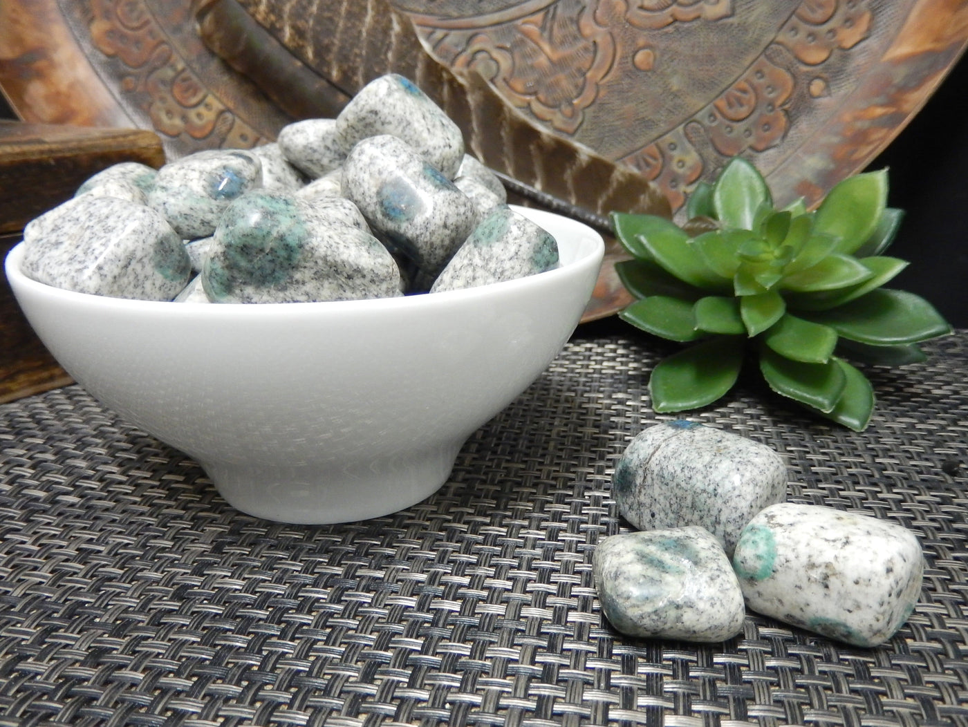 3 granite/jasper stones next to a bowl filled with them with decorations in the background