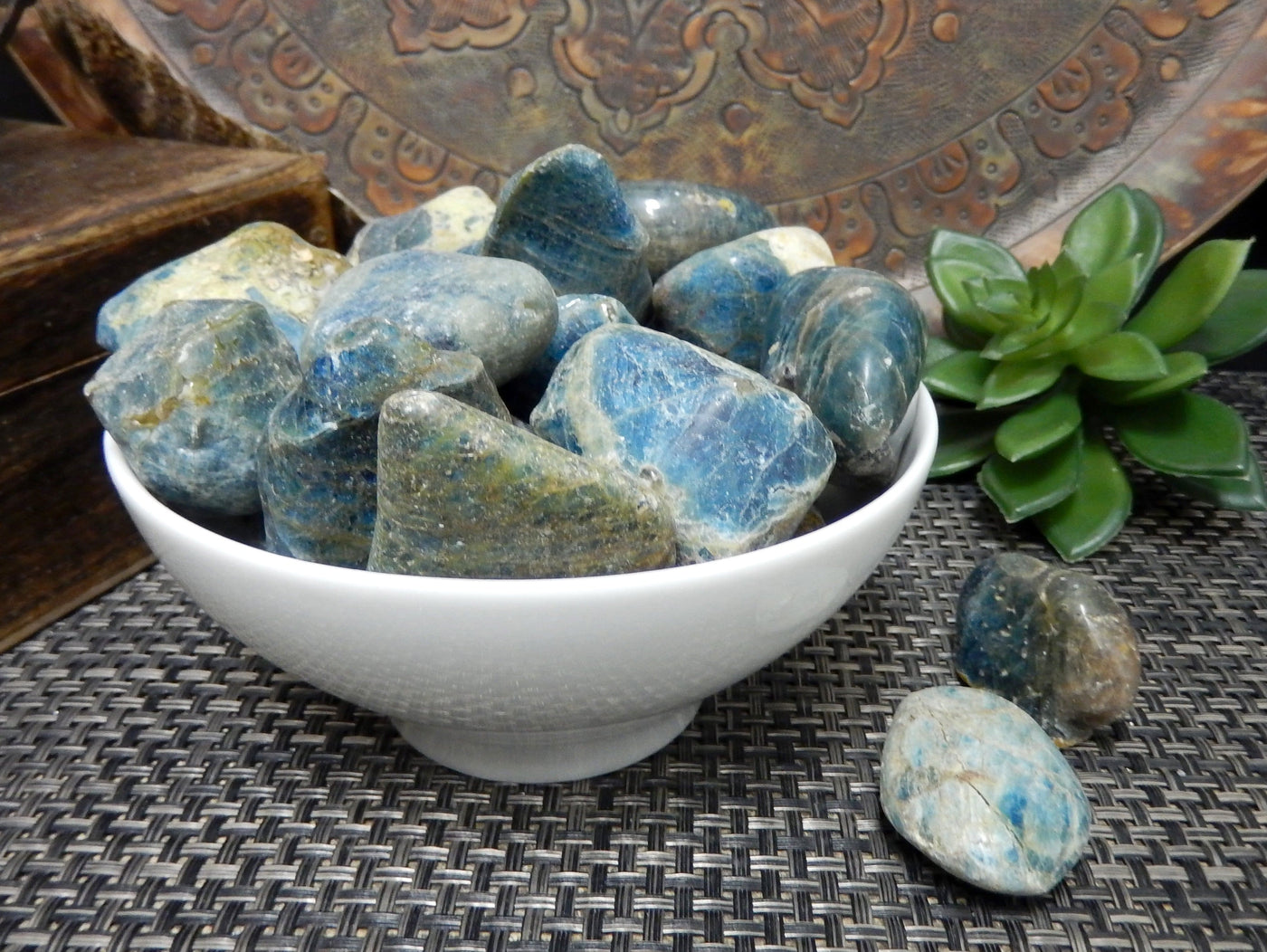 Blue apatite tumbled stones in a white bowl.