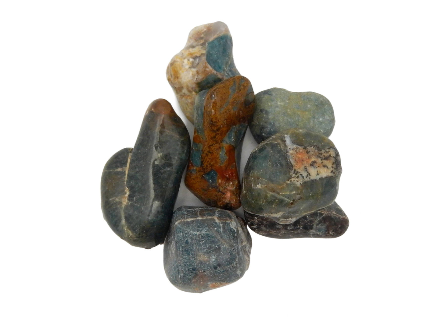 Blue apatite tumbled stones on a white background. Showing they are a dark grayish blue with some brown and cream