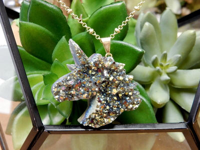 Up close shot of Rainbow Titanium Druzy Unicorn Pendant with gold bail and necklace chain in front of succulents