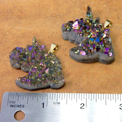 Up close shot of 2 Rainbow Titanium Druzy Unicorn Pendants with gold bails next to ruler for size reference