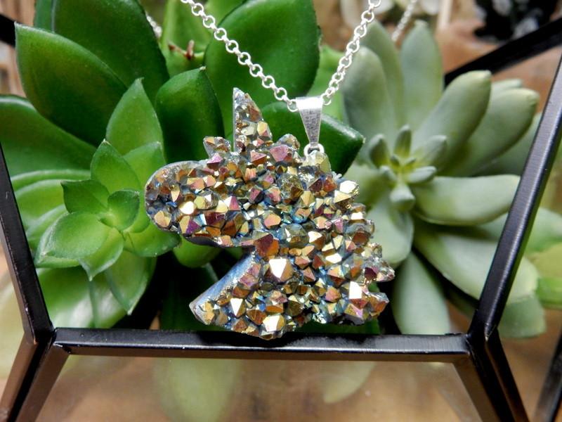 Up close shot of Rainbow Titanium Druzy Unicorn Pendant with silver bail and necklace chain in front of succulents